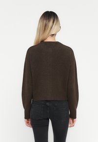 Bruine cropped trui met ribbelboord, lange mouwen en een ronde hals, gecombineerd met donkergrijze, aansluitende jeans. Glad textuur, minimalistisch ontwerp.