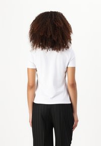 T-shirt bianco a maniche corte, colletto tondo, realizzato in morbido cotone, design aderente, mostrato da dietro, abbinato a pantaloni neri a righe sottili.