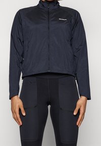 Svart lättviktsjacka med hög krage, hel dragkedja fram och långa ärmar. Har varumärkets logotyp på bröstet och en stilren design.