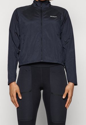 Veste légère noire avec un col montant, fermeture éclair sur toute la longueur et manches longues. Présente le logo de la marque sur la poitrine et un design épuré.