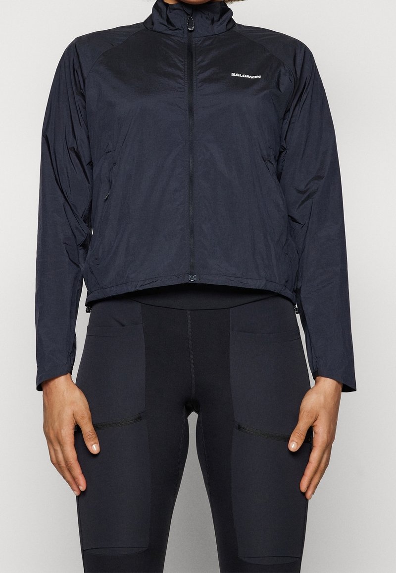 Svart lättviktsjacka med hög krage, hel dragkedja fram och långa ärmar. Har varumärkets logotyp på bröstet och en stilren design.