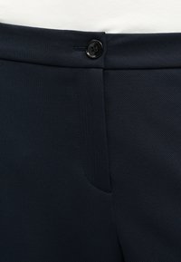 Pantalon bleu marine foncé avec une ceinture boutonnée et un détail de poche avant, en tissu texturé.