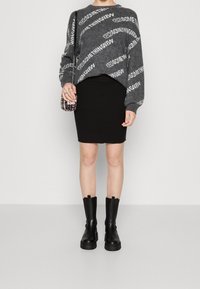 Grå tröja med vit textmönster, ribbad svart kjol och knähöga svarta stövlar. Inkluderar en liten pärlhantverkat handväska.