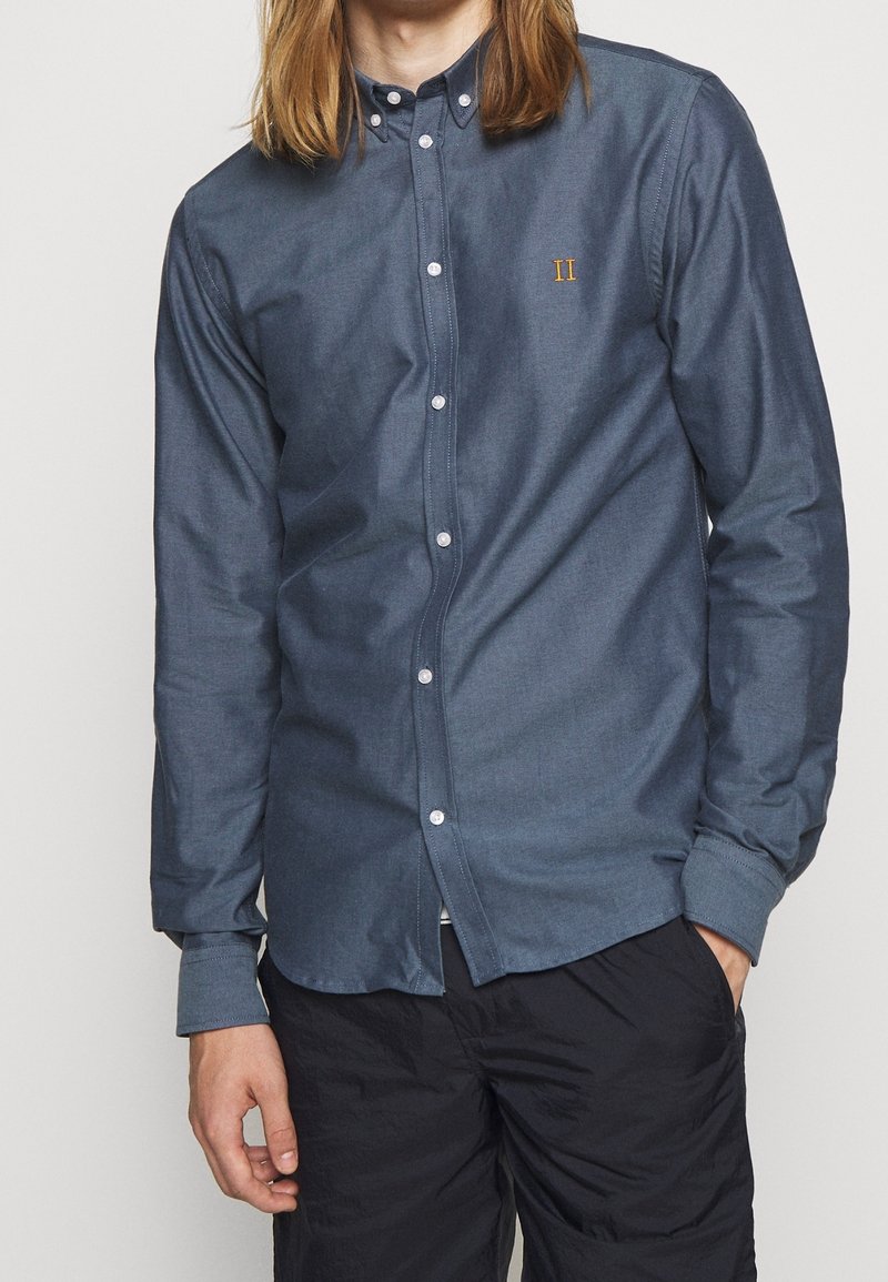 Overhemd van donkerblauwe katoen met lange mouwen, kraag en witte knopen; heeft een kleine geborduurde "II" op de borst.