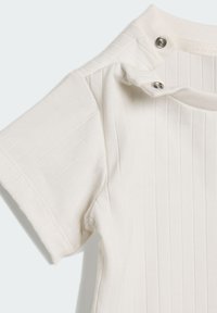 Camiseta blanca de manga corta con tejido acanalado y dos botones a presión plateados en la sisa del hombro.