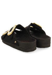 Sandalias negras con acentos dorados, suela plana, plantilla texturizada y correas anchas con embellishments circulares para añadir detalle.