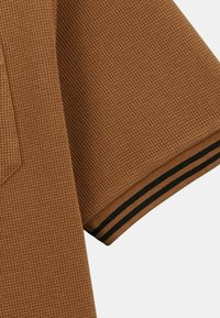 Chemise courte à manches en tissu brun texturé avec un motif tissé. Présente des accents rayés noir et blanc au niveau du poignet.