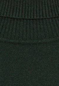 Tamnozeleni pleteni materijal s rebrastom teksturom. Ima vodoravne linije i ujednačeno istezanje kroz cijeli materijal.