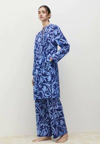 Blauw gestippeld loungewear set bestaande uit een langslavige top met ritssluiting en bijpassende wijde broek. De stof heeft een soepele textuur.