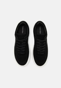 Baskets en daim noir avec un design perforé, des lacets plats noirs et des semelles en caoutchouc blanches. Dotées d'une semelle intérieure de marque et d'un logo subtil.