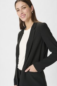 Blazer nero dal design elegante, con chiusura a un bottone e tasche laterali, abbinato a un top bianco con una texture di tessuto liscia.
