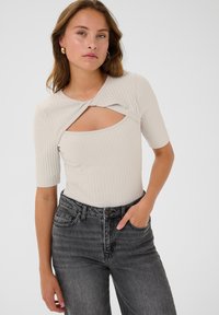 Lichtbeige geribbelde bodysuit met korte mouwen en een gedraaid uitsnijdontwerp aan de voorkant, gecombineerd met hooggerokte donkergrijze jeans. Smoothe textuur.