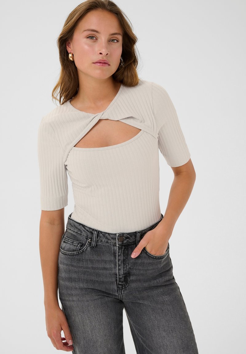 Lichtbeige geribbelde bodysuit met korte mouwen en een gedraaid uitsnijdontwerp aan de voorkant, gecombineerd met hooggerokte donkergrijze jeans. Smoothe textuur.