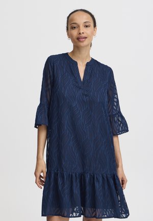 Navyblaues Kleid mit einem geschichteten Rüschensaum, das ein strukturiertes Wellenmuster aufweist, einen V-Ausschnitt und Glockenärmel hat. Leichtes, halbtransparentes Material.