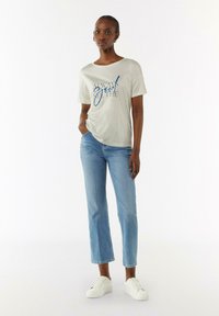 Light grey t-shirt with blue lettering, relaxed fit, paired with mid-rise blue jeans and white sneakers. Smooth fabric and straight leg design.