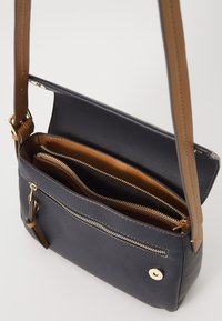 Borsa a tracolla in pelle blu navy con tracolla marrone, dotata di una tasca con zip sul davanti, svariati scomparti interni e dettagli in hardware color oro.
