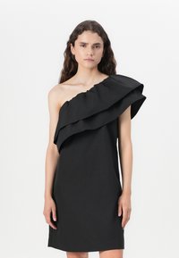 Svart en-skulder kjole med en stor volangdetalj over brystet, laget av et glatt stoff med en elegant, tett silhuett.
