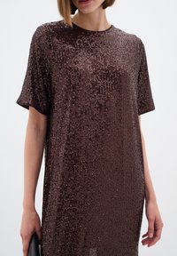 Barna flitteres ruha rövid ujjakkal, sima textúrával és függőleges csillogó mintával, fekete clutch táskával párosítva.