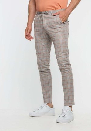 Pantaloni a scacchi grigi con righe arancioni, tessuto leggero, vita elastica con cordino, indossati con sneakers bianche.