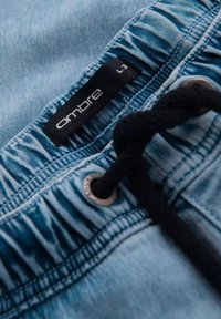 Pantalones cortos de mezclilla con un lavado azul claro, cinturilla fruncida, cordón negro y ojetes metálicos. La etiqueta dice "ombre" con talla L3.