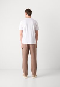 Hvit t-skjorte med korte ermer og lysebrune bukser, med en avslappet passform. Egenskaper inkluderer et enkelt design og ensartet tekstur, kombinert med beige fottøy.