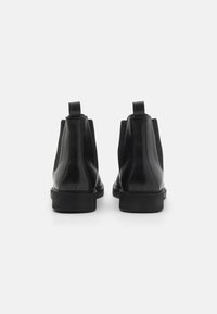 Bottines noires en cuir avec des panneaux élastiques latéraux, finition lisse, bout arrondi et semelles en caoutchouc épaisses. Comprend des tirettes à l'arrière.