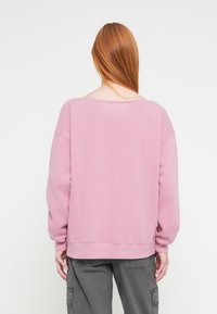 Rózsaszín pulóver laza szabással, széles nyakkivágással és hosszú ujjakkal. Bordázott passzékkal az ujjvégeken és az alján, puha anyagú textúrával.