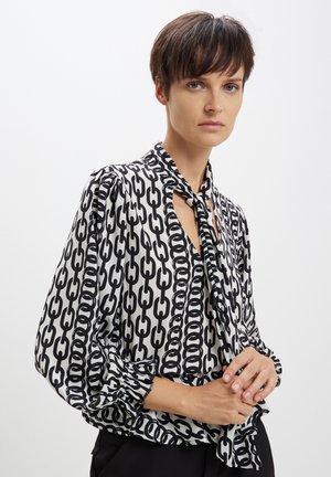 Blusa bianca e nera con motivo a catena, dotata di scollo con fiocco e maniche a sbuffo con polsini arricciati. Tessuto morbido e leggero.