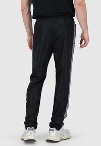 Schwarze Sporthose aus glattem Material, mit schmaler Passform, elastischem Bund und grauen seitlichen Streifen mit einem Logomuster.