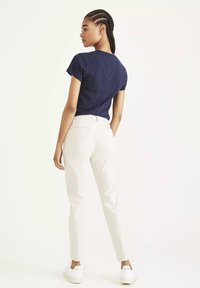 Námornícky modré tričko s krátkym rukávom, svetlo béžové slim-fit nohavice a biele tenisky. Model stojí chrbtom, ukazuje štruktúrovaný vrch a priliehavý spodok.