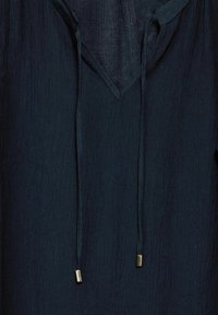 Blusa blu navy, con texture e scollo a V, caratterizzata da lacci regolabili con punte metalliche. Il tessuto presenta un apparente effetto leggermente stropicciato.