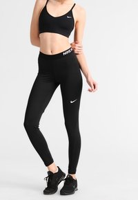 Svart idrottsbehå och leggins gjorda av elastisk tyg. Behå har tunna axelband, leggins har hög midja och Nike-logotyp i vitt.