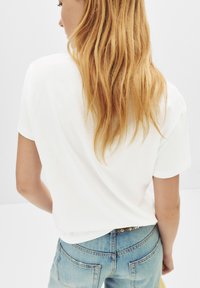T-shirt en coton blanc avec une coupe décontractée, des manches courtes et un ourlet arrondi, associé à un jean en denim bleu avec des poches arrière.