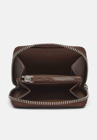Kompaktowy brązowy skórzany portfel otwarty, ukazujący dwie główne przegrody i centralną kieszeń na zamek błyskawiczny z metalowymi zębami w kolorze srebrnym.