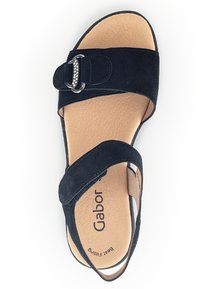 Zwarte suède sandaal met een brede band, een decoratieve zilveren gesp en een gewatteerde beige binnenzool. Beschikt over een platte zool en een open te ontwerp.