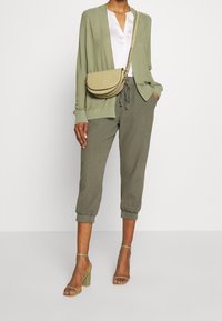 Cardigan vert olive, blouse blanche et pantalon fuselé vert olive. Accessoirisé d'un petit sac bandoulière et de sandales à talons carrés verts.