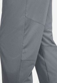 Grijze broek met een gladde stof, voorzien van een gestructureerd mesh paneel op het bovenbeen. De stiksels zijn netjes met praktische designelementen.