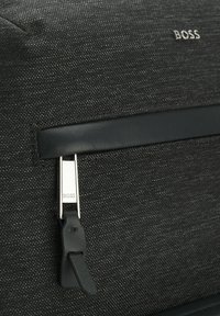 Borsa di tessuto nera caratterizzata da una superficie testurizzata, una striscia di accentuazione in pelle e accessori in argento con il logo "BOSS" impresso.