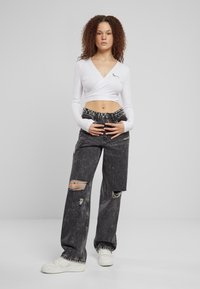 Biely dlhý rukáv cropped top s v-výstrihom; čierne roztrhnuté široké nohavice; biele tenisky; textúrované vlasy; neutrálny pozadie.