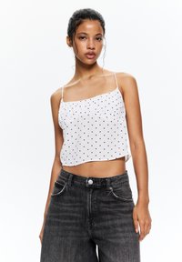 Fehér cropped top piros pöttyökkel, vékony pántokkal és gyűrött részletekkel. Magas derekú fekete farmernadrággal viselve, gombos záródással.