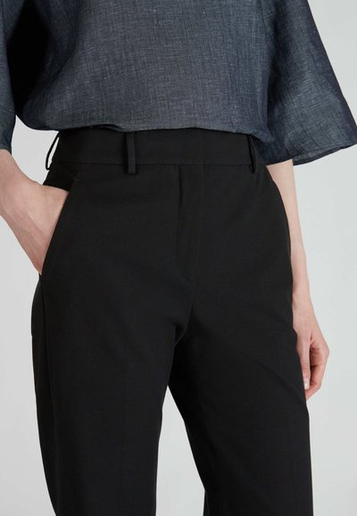 Zwarte broek van een gladde stof, met zijzakken, een getailleerde pasvorm en een platte voorkant. Gecombineerd met een gestructureerde, donkerblauwe top.