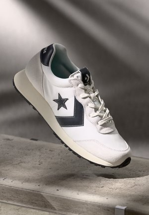 White sneaker with navy accents, rubber sole, and textured materials. Features a star logo and simple lace-up design.
