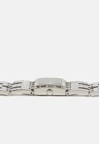 Montre-bracelet rectangulaire en argent avec un bracelet à motif, présentant un cadran sombre, des accents métalliques et des pierres décoratives incrustées.