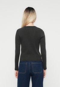Mørk grå langermet ribbestrikket topp med rund hals, paret med blå høytlivsjeans med to baklommer.