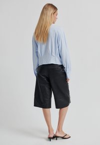 Světlomodrá krátká košile s dlouhými rukávy ve spojení s černými koženými šortkami, zdůrazňující hladkou texturu a minimalistický design.