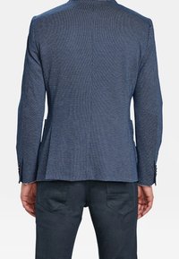 Mörkblå texturerad blazer med skräddarsydd passform, med ventilerad rygg och knappdetaljer på ärmarna, tillsammans med mörka byxor.