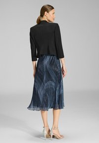 Czarna krótka kurtka z rękawami trzy czwarte, w połączeniu z niebieską spódnicą w wzory, która ma płynne tekstury i krój opadający poniżej kolana.