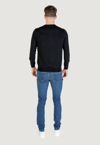 Maglione nero a maniche lunghe, design aderente, indossato sopra jeans azzurri chiari, vista da dietro, sneakers bianche, texture del tessuto liscia.
