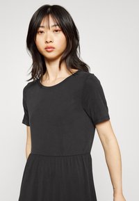 Vestido preto de mangas curtas em tecido suave com decote redondo e cintura franzida. Textura suave e design simples e aerodinâmico.