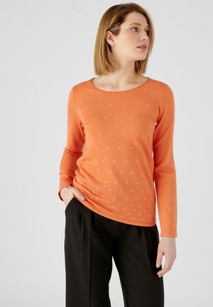 Camicia a maniche lunghe arancione con scollo a barca, caratterizzata da un motivo sottile di piccole macchie argento. Tessuto morbido, abbinata a pantaloni neri.